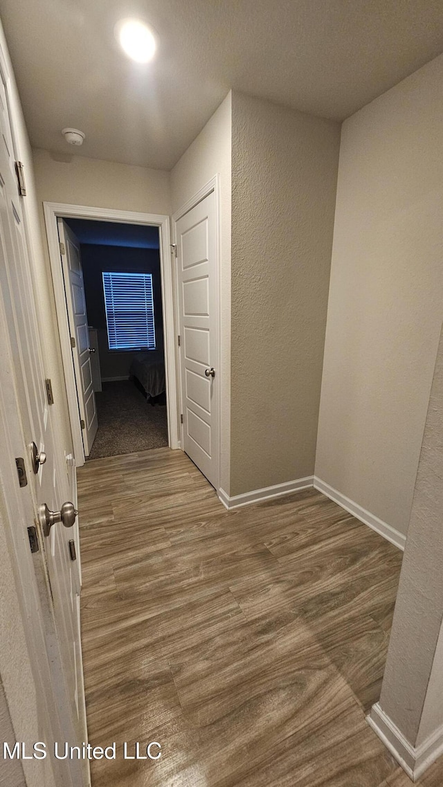 hallway with a textured wall, wood finished floors, and baseboards