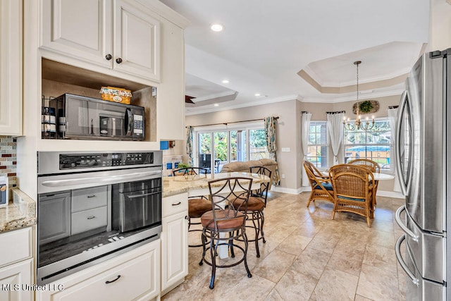 kitchen featuring appliances with stainless steel finishes, white cabinets, light stone countertops, and a tray ceiling