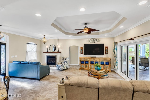 living room with a wealth of natural light, ornamental molding, a tiled fireplace, and a raised ceiling