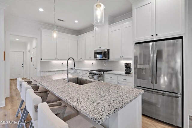 kitchen with stainless steel appliances, sink, decorative light fixtures, white cabinets, and a center island with sink