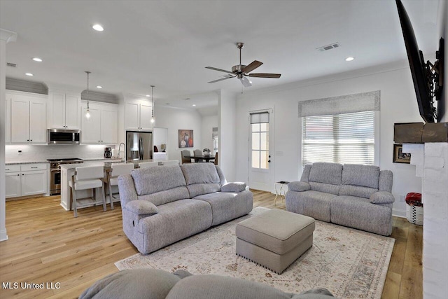 living room with sink, light wood-type flooring, ceiling fan, and ornamental molding