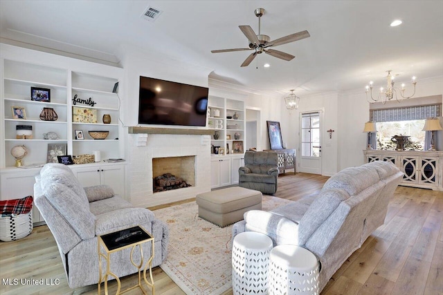 living room featuring built in shelves, light wood-type flooring, ceiling fan with notable chandelier, a fireplace, and ornamental molding