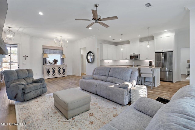 living room with ceiling fan with notable chandelier, ornamental molding, and light hardwood / wood-style floors