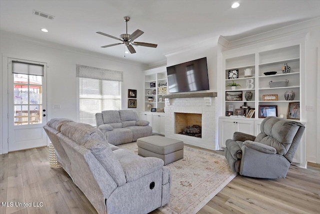 living room featuring a brick fireplace, built in features, ceiling fan, and crown molding