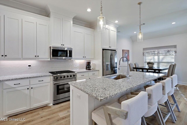 kitchen featuring hanging light fixtures, an island with sink, a kitchen bar, white cabinets, and appliances with stainless steel finishes