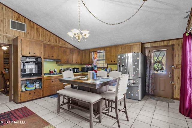 kitchen with wooden walls, visible vents, lofted ceiling, brown cabinets, and black appliances