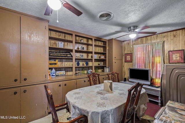 dining room with visible vents, wood walls, a textured ceiling, and ceiling fan