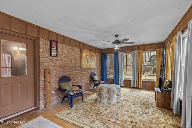 sitting room with a ceiling fan, wood walls, and brick wall