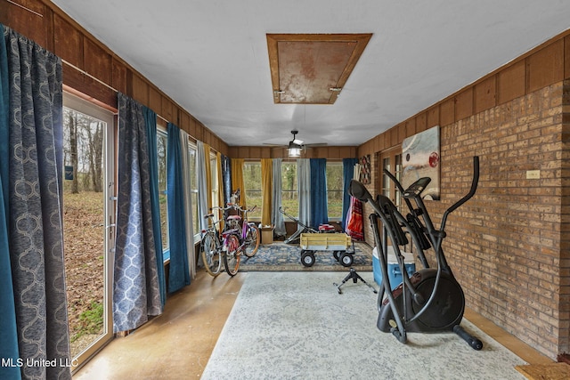 workout area featuring attic access, a sunroom, wood walls, and brick wall