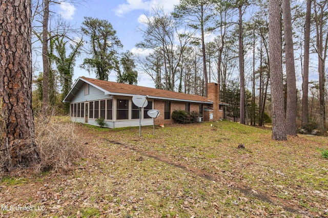 view of front of house featuring a sunroom, a chimney, and brick siding