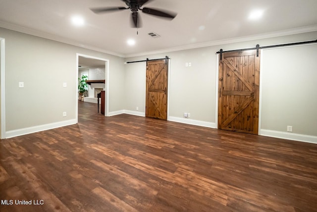 unfurnished bedroom with a barn door, dark wood-style floors, ornamental molding, and baseboards