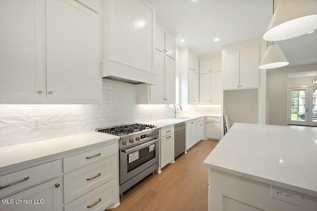 kitchen with a sink, appliances with stainless steel finishes, white cabinetry, backsplash, and light wood-style flooring