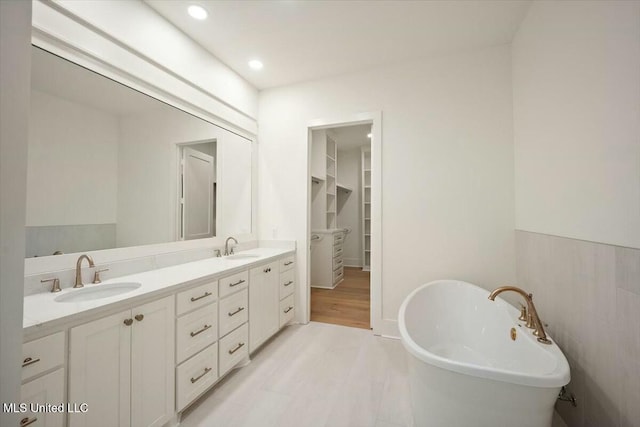 bathroom featuring a sink, a walk in closet, double vanity, and a soaking tub