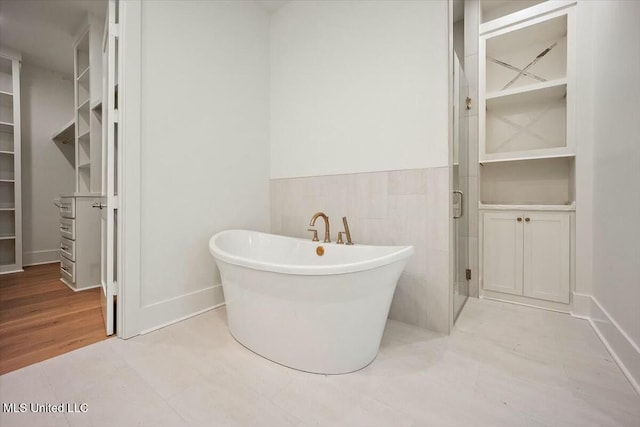 bathroom featuring a freestanding tub, a spacious closet, a shower stall, wainscoting, and tile walls