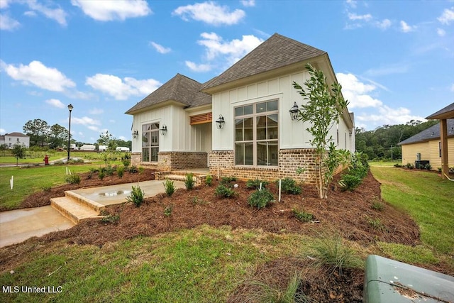 view of front of house with roof with shingles, a patio area, a front lawn, and brick siding