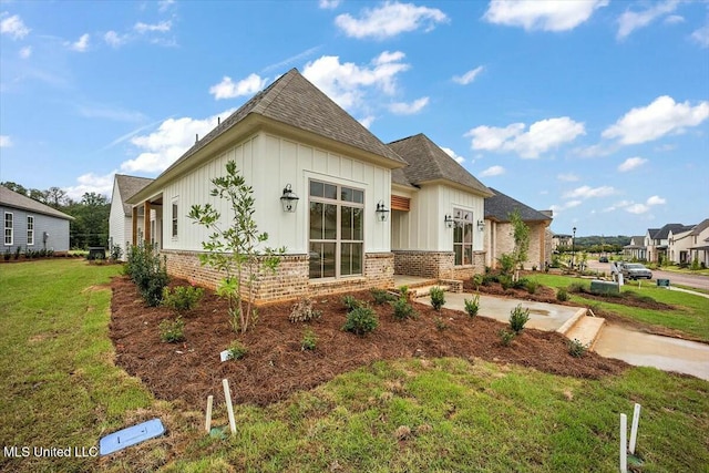 view of front of house with a shingled roof, brick siding, board and batten siding, and a front lawn