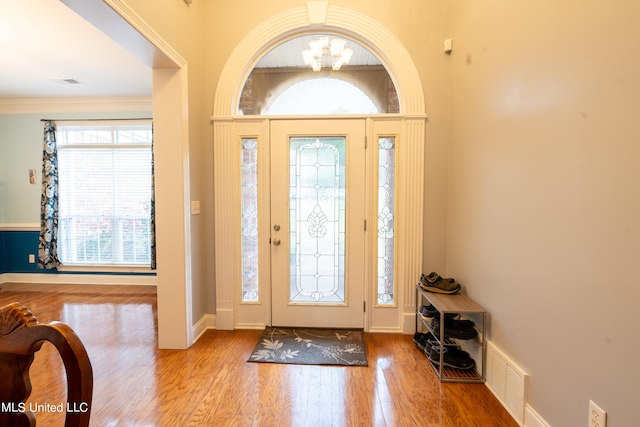 foyer featuring crown molding, light hardwood / wood-style flooring, an inviting chandelier, and plenty of natural light