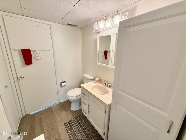 half bathroom featuring visible vents, a drop ceiling, toilet, wood finished floors, and vanity