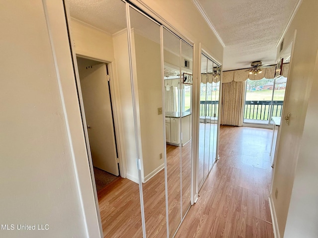 corridor with light wood-style flooring, ornamental molding, and a textured ceiling