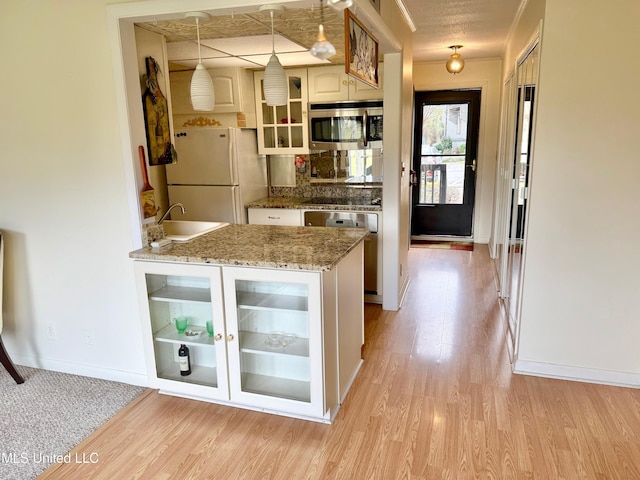 kitchen featuring stainless steel microwave, light wood-style flooring, glass insert cabinets, freestanding refrigerator, and a sink