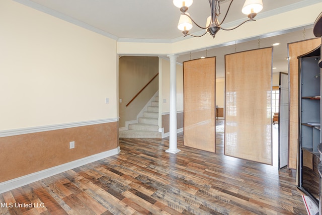 spare room featuring an inviting chandelier, ornamental molding, dark hardwood / wood-style flooring, and decorative columns