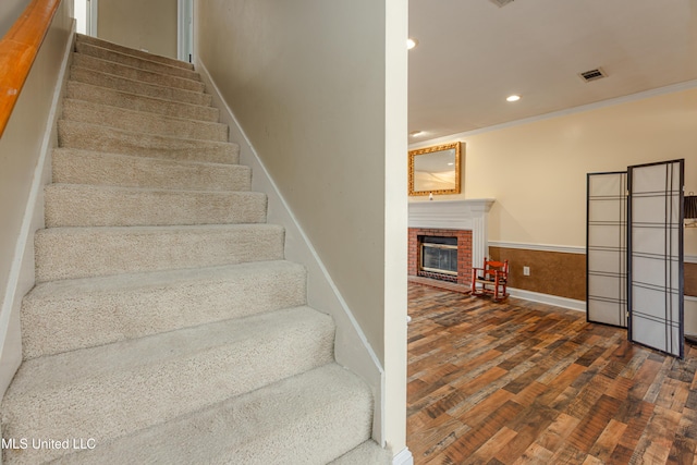 stairway with hardwood / wood-style flooring, ornamental molding, and a fireplace