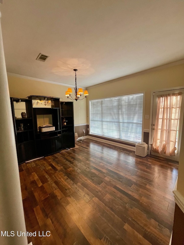 unfurnished living room with an inviting chandelier, dark wood-type flooring, and ornamental molding