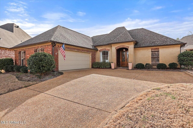 french country inspired facade with brick siding, driveway, an attached garage, and roof with shingles