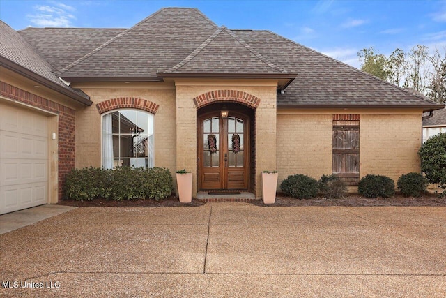 doorway to property with a garage, a shingled roof, french doors, and brick siding