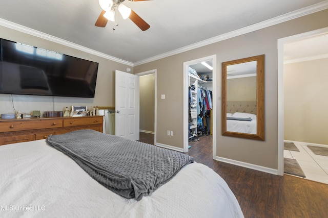 bedroom with a spacious closet, ornamental molding, baseboards, and wood finished floors