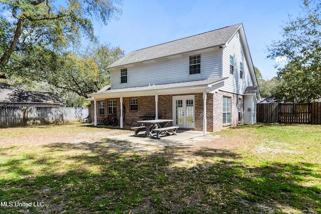 rear view of house featuring brick siding, french doors, a fenced backyard, a yard, and a patio