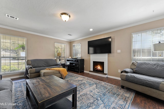 living room featuring visible vents, crown molding, baseboards, a lit fireplace, and wood finished floors