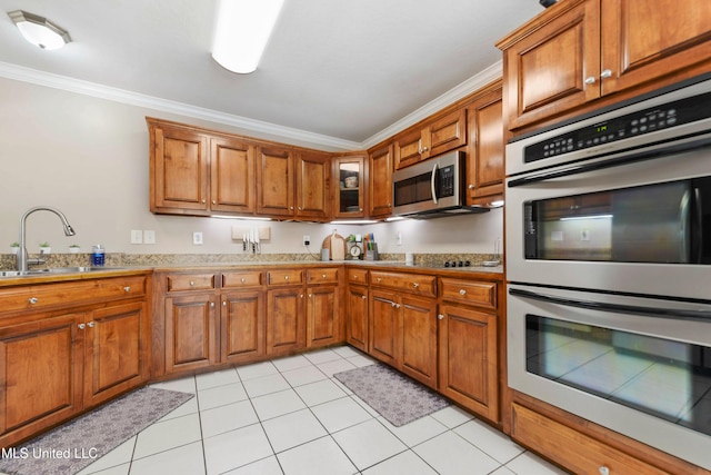 kitchen with a sink, appliances with stainless steel finishes, ornamental molding, and brown cabinetry