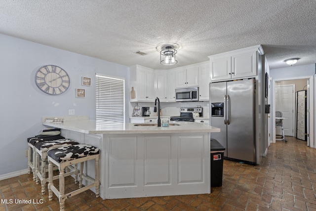 kitchen featuring sink, stainless steel appliances, white cabinets, a kitchen bar, and kitchen peninsula