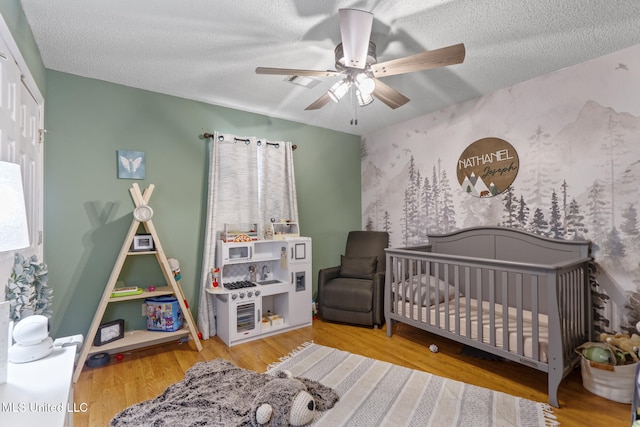 bedroom with wood-type flooring, a textured ceiling, and a crib