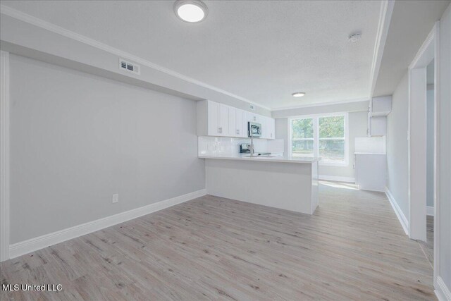 250 1st St, Webb, MS 38966 - kitchen with a peninsula, stainless steel microwave, light wood-style floors, white cabinetry, and crown molding