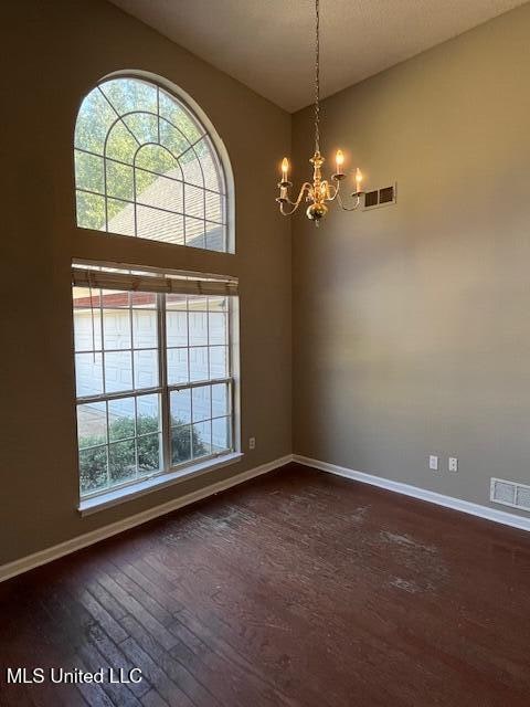 spare room featuring an inviting chandelier, dark hardwood / wood-style floors, and a high ceiling