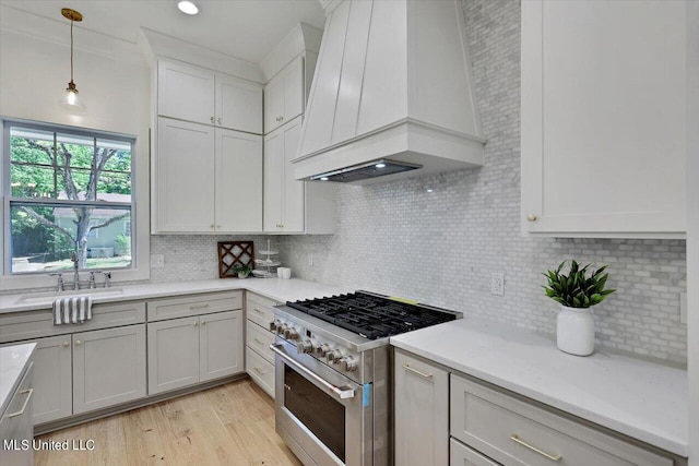 kitchen with tasteful backsplash, premium range hood, light wood-type flooring, high end stainless steel range, and pendant lighting