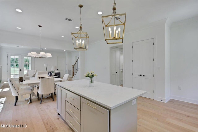 kitchen featuring light stone countertops, a center island, decorative light fixtures, and light hardwood / wood-style floors