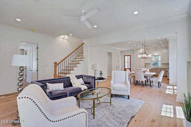 living room featuring crown molding, ceiling fan with notable chandelier, and light wood-type flooring