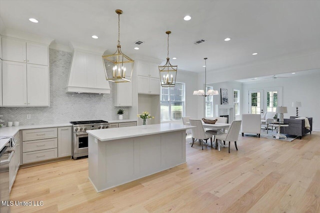 kitchen with pendant lighting, premium range hood, light hardwood / wood-style flooring, and stainless steel range