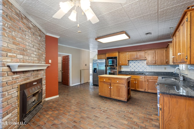 kitchen with a kitchen island, sink, crown molding, a brick fireplace, and appliances with stainless steel finishes