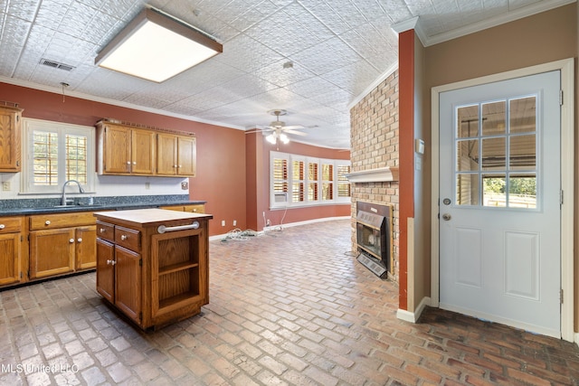 kitchen with ornamental molding, a center island, a brick fireplace, and ceiling fan