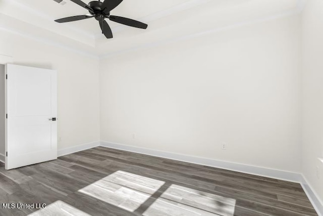 empty room with a ceiling fan, a tray ceiling, baseboards, and wood finished floors