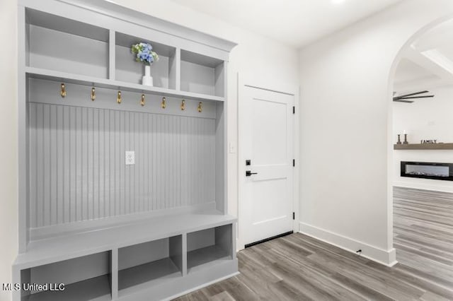 mudroom with baseboards, a fireplace, arched walkways, and wood finished floors