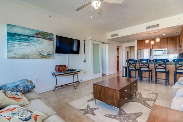 living room with a ceiling fan, visible vents, and a textured ceiling