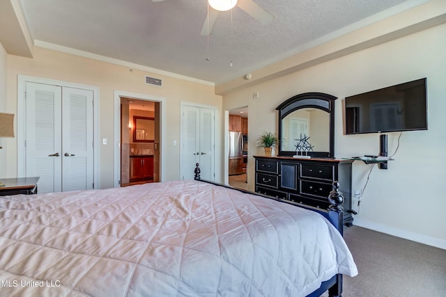 carpeted bedroom with a textured ceiling, ceiling fan, visible vents, baseboards, and two closets