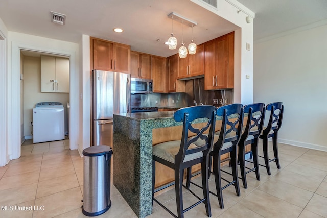 kitchen with washer / dryer, light tile patterned floors, visible vents, brown cabinetry, and stainless steel appliances