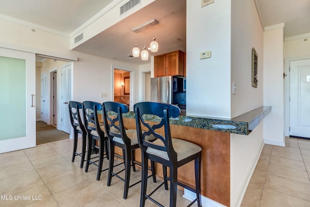 kitchen featuring light tile patterned floors, a kitchen breakfast bar, hanging light fixtures, freestanding refrigerator, and brown cabinets