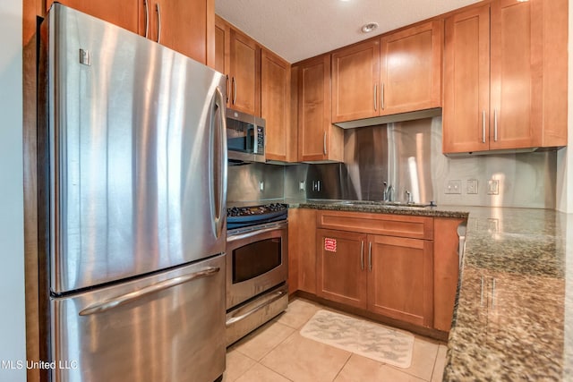 kitchen with brown cabinets, appliances with stainless steel finishes, dark stone counters, and a sink